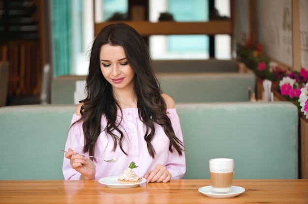 Jovem mulher feliz atrativa que senta e que come a sobremesa no café.