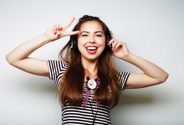 Jovem mulher feliz com fones de ouvido ouvindo música sobre fundo cinza