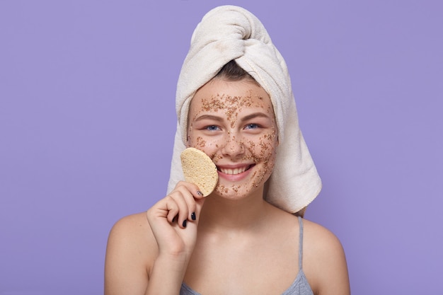 Foto jovem mulher feliz com máscara facial hidratante, possui esponja para remover maquiagem