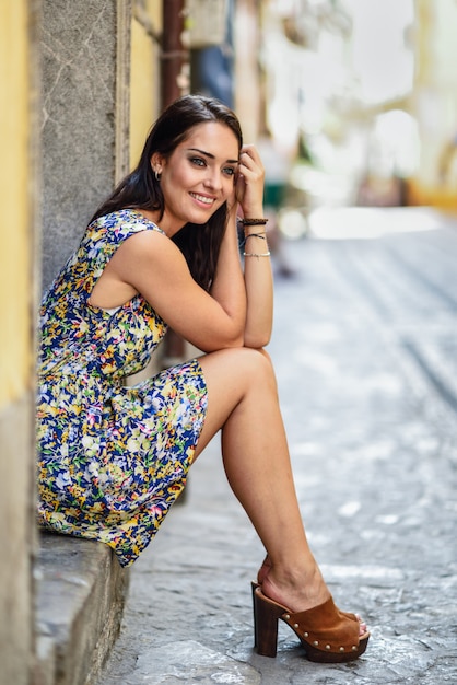 Jovem mulher feliz com olhos azuis que sorri sentando-se na etapa urbana.