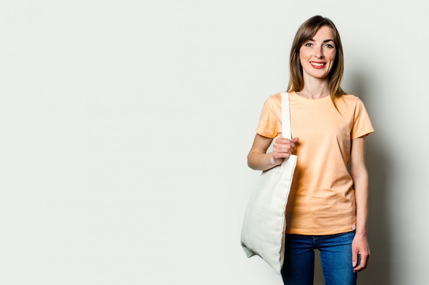 Jovem mulher feliz com uma sacola de compras no ombro em uma luz de fundo