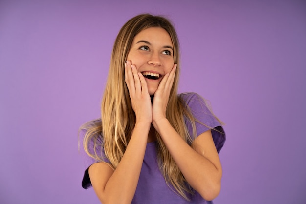 Foto jovem mulher feliz e surpresa, olhando para cima e segurando as bochechas com as mãos em pé contra um fundo isolado.