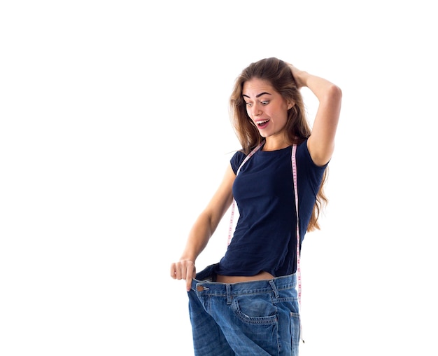 Jovem mulher feliz em camiseta com centímetro em volta do pescoço segurando seu jeans de tamanho muito maior