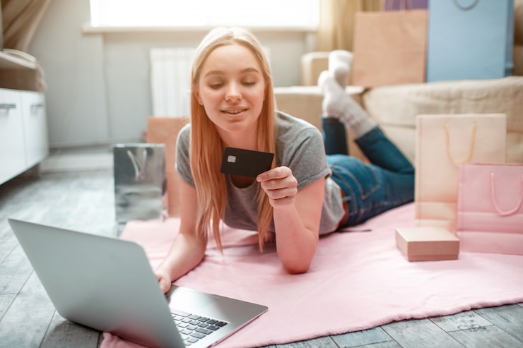 Foto jovem mulher feliz ia pronto para gastar dinheiro com cartão de banco do marido enquanto estava deitado no chão com sacos de compras