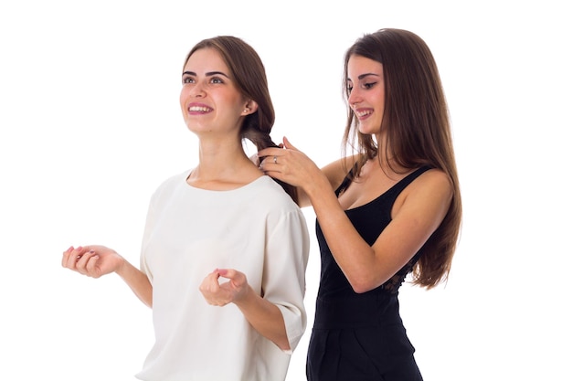 Jovem mulher feliz na camisa preta fazendo outra mulher sorridente na camisa branca uma trança no estúdio