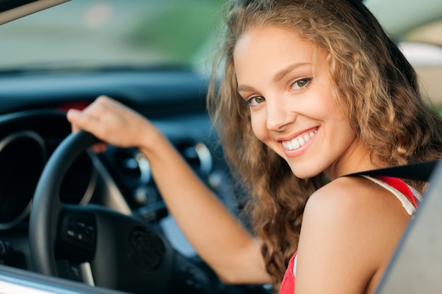 Jovem mulher feliz num carro sorrindo - conceito de comprar carro