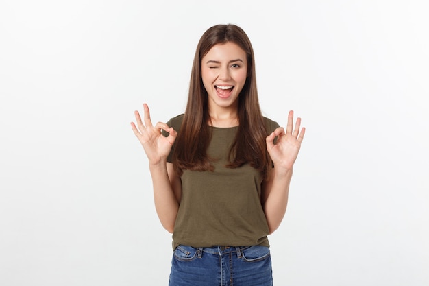 Jovem mulher feliz que mostra o sinal aprovado com dedos uma piscadela isolada em um fundo cinzento.