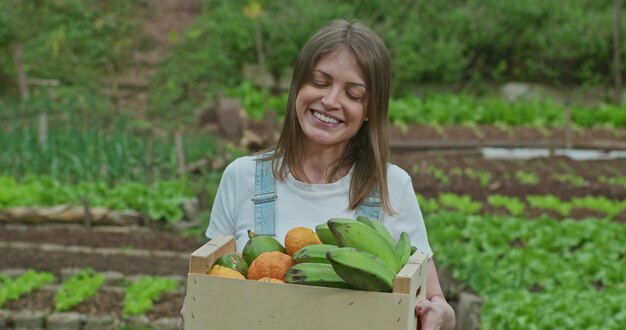 Foto jovem mulher feliz segurando cesta de frutas e legumes do lado de fora em campo verde uma agricultora proprietária de uma pequena empresa detém bananas e tangerinas