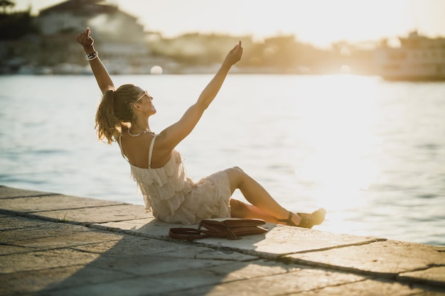 Jovem mulher feliz sentada à beira-mar enquanto desfruta de umas férias de verão.