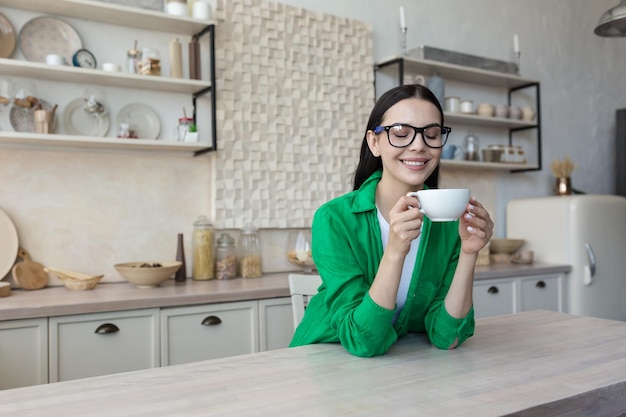 Jovem mulher feliz tomando café na cozinha pela manhã