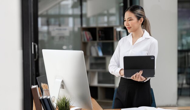 Jovem mulher feliz trabalhando em tablet e computador desktop no escritório