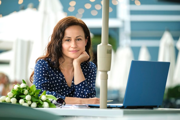 Jovem mulher feliz trabalhando remotamente no laptop sentado na mesa do restaurante ao ar livre Fazendo negócios on-line conceito