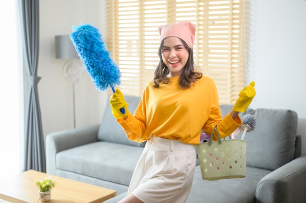 Jovem mulher feliz usando luvas amarelas e segurando uma cesta de material de limpeza na sala de estar