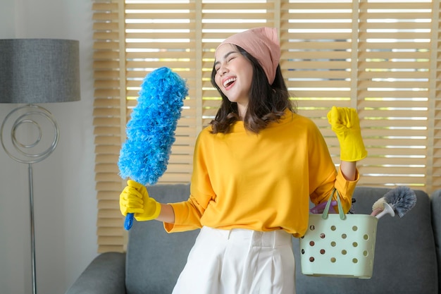 Jovem mulher feliz usando luvas amarelas e segurando uma cesta de material de limpeza na sala de estar