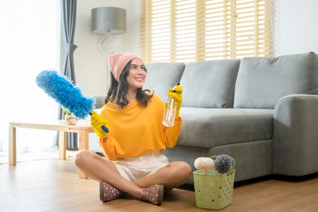 Jovem mulher feliz usando luvas amarelas e segurando uma cesta de material de limpeza na sala de estar