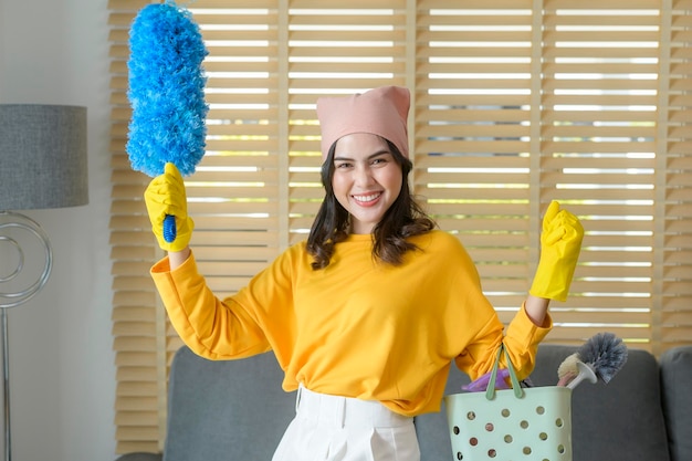 Jovem mulher feliz usando luvas amarelas e segurando uma cesta de material de limpeza na sala de estar