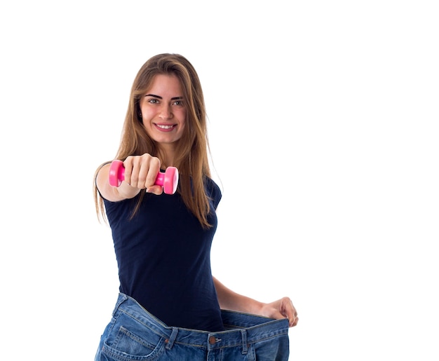 Jovem mulher feliz vestindo camiseta azul e jeans de tamanho muito maior, segurando o haltere rosa