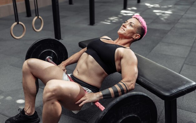 Jovem mulher forte atlética praticando exercício de ponte de glúteo com uma barra pesada nas pernas dela. Musculação e Fitness