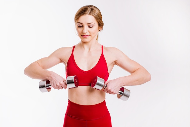 Jovem mulher forte e esportiva em pano vermelho fazendo exercícios com halteres em fundo branco