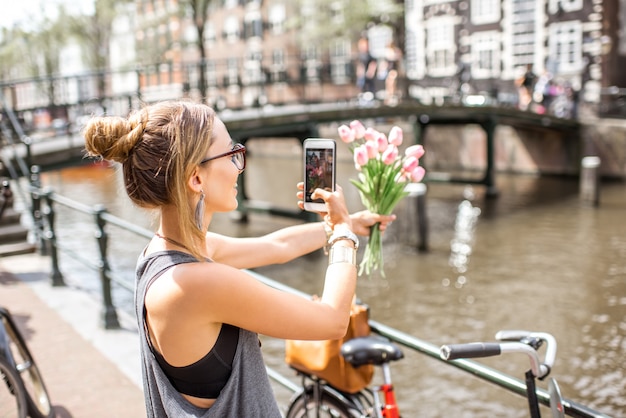 Jovem mulher fotografando com telefone lindo buquê de tulipas cor de rosa no fundo da cidade em Amsterdã