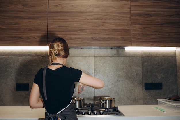 Jovem mulher fritando ovos no café da manhã no fogão de cozinha vista de trás