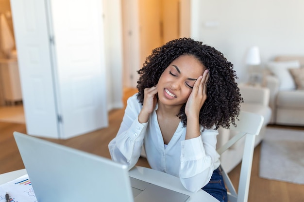 Jovem mulher frustrada trabalhando na mesa de escritório na frente do laptop que sofre de tratamento de dores de cabeça diárias crônicas on-line, nomeando para uma consulta médica pagamento por doença de radiação eletromagnética