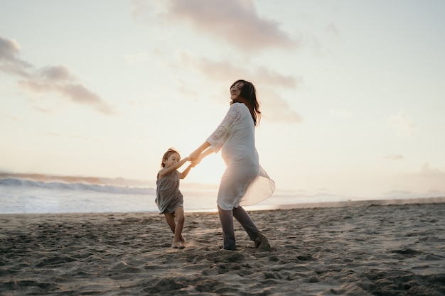 Jovem mulher grávida bonita com sua filha bonita brincando na praia