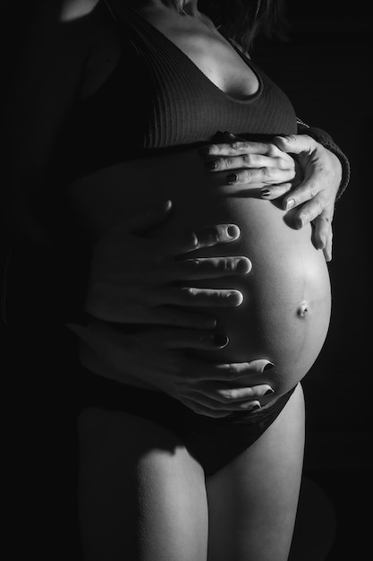 Jovem mulher grávida caucasiana prestes a dar à luz Com as mãos de seu pai e sua mãe na barriga do bebê Em algumas fotos de estúdio fotos em preto e branco