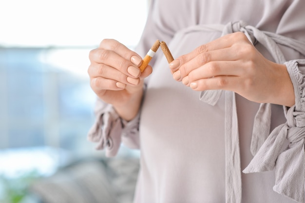 Jovem mulher grávida com cigarro quebrado, closeup. Conceito de recusa por mau hábito