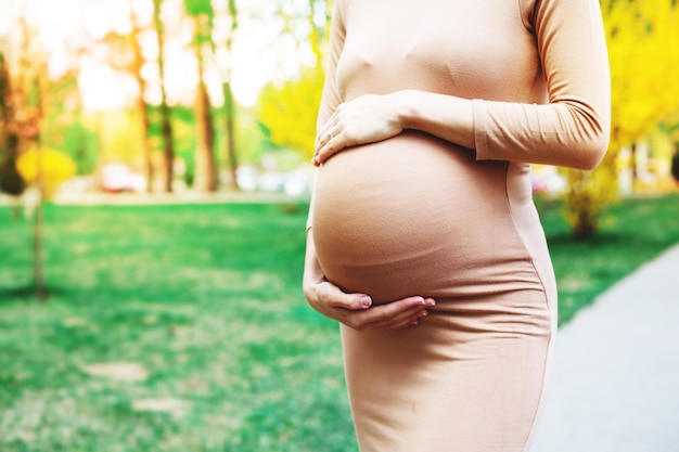 Jovem mulher grávida de pé ao ar livre no parque da cidade e segurando sua barriga maternidade gravidez pessoas e expectativa conceito