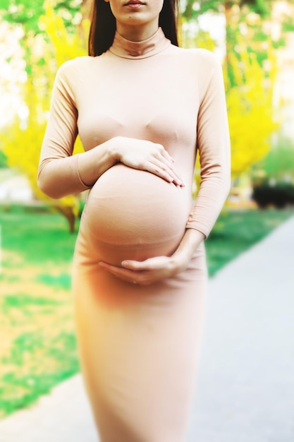 Jovem mulher grávida de pé ao ar livre no parque da cidade e segurando sua barriga maternidade gravidez pessoas e expectativa conceito