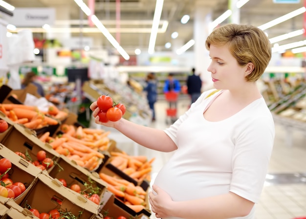 Jovem mulher grávida escolhendo tomate fresco no supermercado