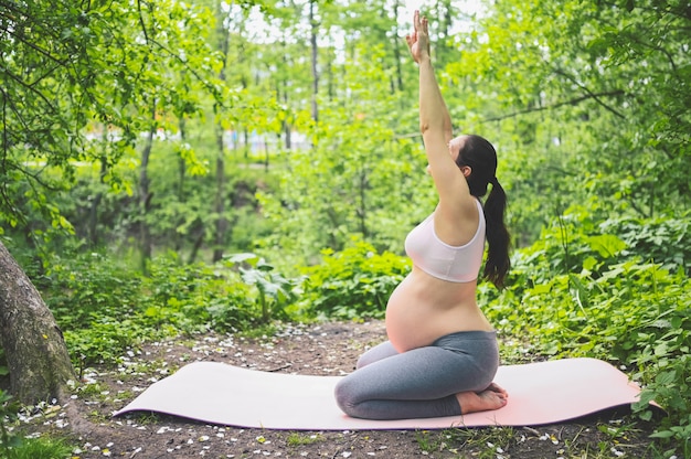 jovem mulher grávida fazendo yoga exercícios no parque ao ar livre