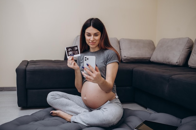 Jovem mulher grávida feliz com ultrassom do bebê na mão falando on-line em tablet digital tendo chamada de vídeo com a família sorrindo feminina mostrando ultrassonografia do embrião para o marido via internet Gravidez