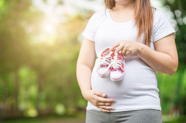 Jovem, mulher grávida, segurando, sapatos bebê, para, dela, barriga