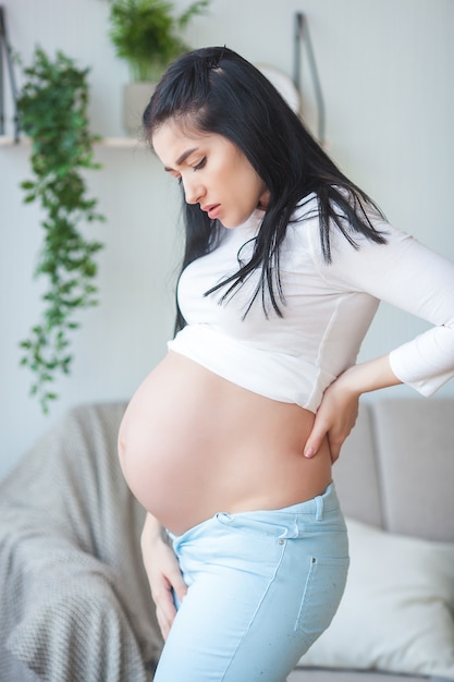 Jovem mulher grávida tendo uma dor nas costas. Esperando mulher se sentindo mal. Mulher grávida que sofre de dor.