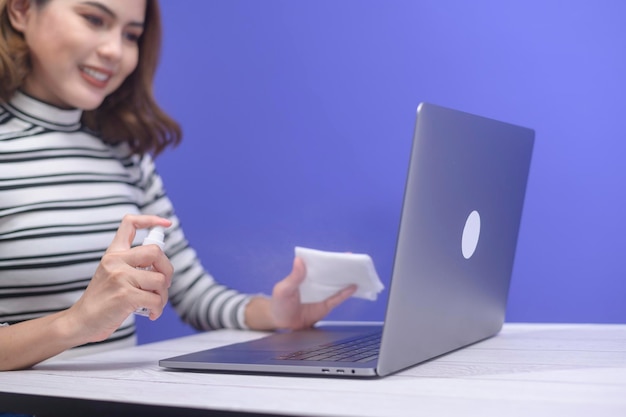 Jovem mulher higienizando spray de álcool com computador, conceito de proteção covid-19.