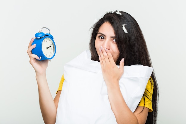 Foto jovem mulher hispânica, acordando segurando um travesseiro e um despertador