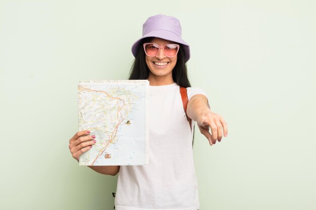 jovem mulher hispânica apontando para a câmera escolhendo seu conceito de turista e mapa