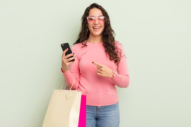 Foto jovem mulher hispânica bonita olhando animada e surpresa apontando para o conceito de sacolas de compras laterais