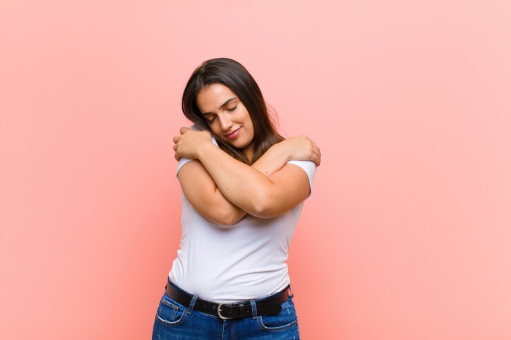 Foto jovem mulher hispânica bonita se apaixonando, sorrindo, abraçando e abraçando a si mesma, permanecendo solteira, sendo egoísta e egocêntrica contra a parede rosa