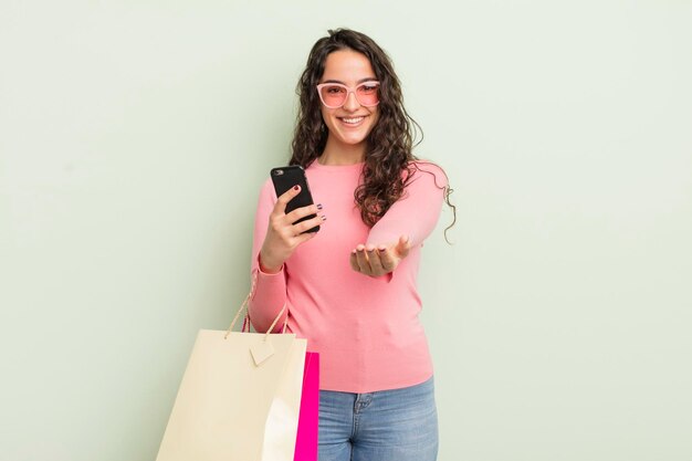 Jovem mulher hispânica bonita sorrindo alegremente com amigável e oferecendo e mostrando um conceito de conceito de sacolas de compras