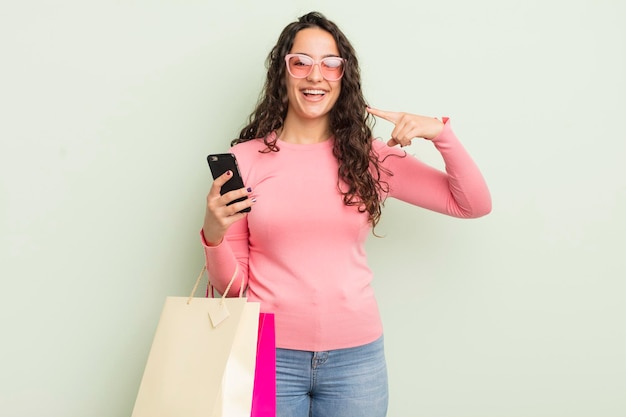 Jovem mulher hispânica bonita sorrindo com confiança apontando para próprio sorriso largo. conceito de sacolas de compras