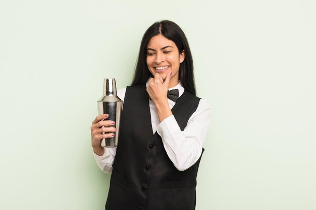 Jovem mulher hispânica bonita sorrindo com uma expressão feliz e confiante com a mão no conceito de barman de coquetel de queixo