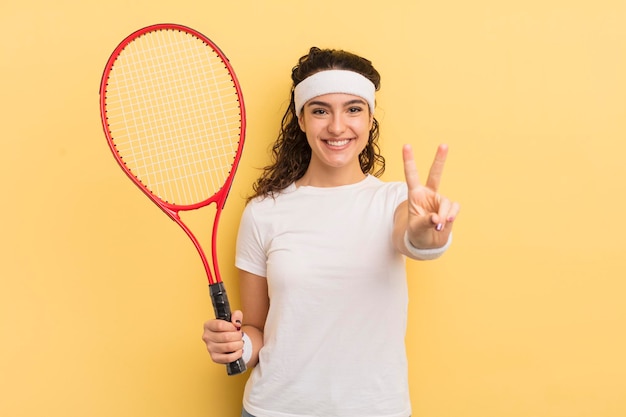 Jovem mulher hispânica bonita sorrindo e olhando feliz gesticulando vitória ou conceito de tênis de paz