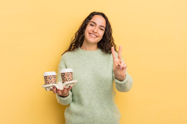 Jovem mulher hispânica bonita sorrindo e parecendo amigável mostrando o conceito de café para tirar o número dois