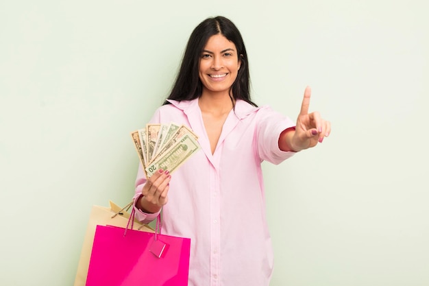 Jovem mulher hispânica bonita sorrindo e parecendo amigável, mostrando o conceito de sacolas de compras número um