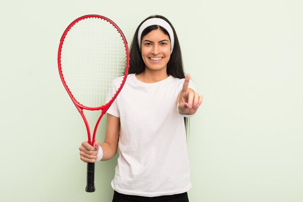 Jovem mulher hispânica bonita sorrindo e parecendo amigável, mostrando o conceito de tênis número um