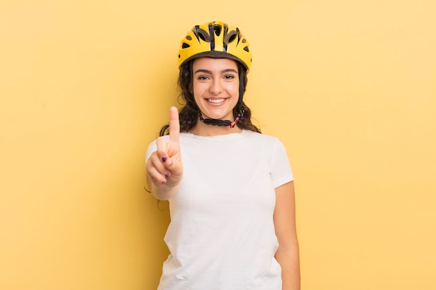 Jovem mulher hispânica bonita sorrindo e parecendo amigável, mostrando o número um. conceito de bicicleta