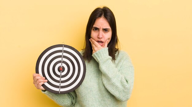 Foto jovem mulher hispânica com boca e olhos bem abertos e mão no conceito de alvo de dardos de queixo